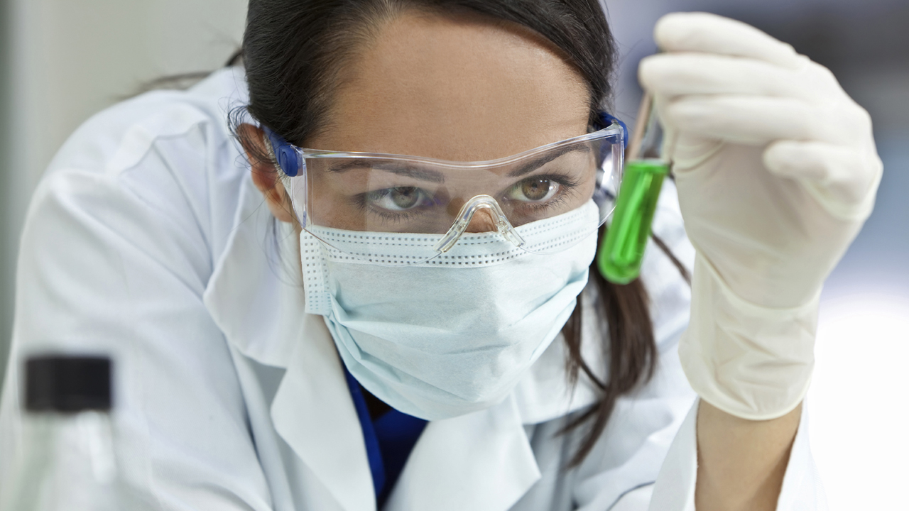 A medical or scientific researcher or doctor looking at a test tube of liqud green solution in a laboratory
